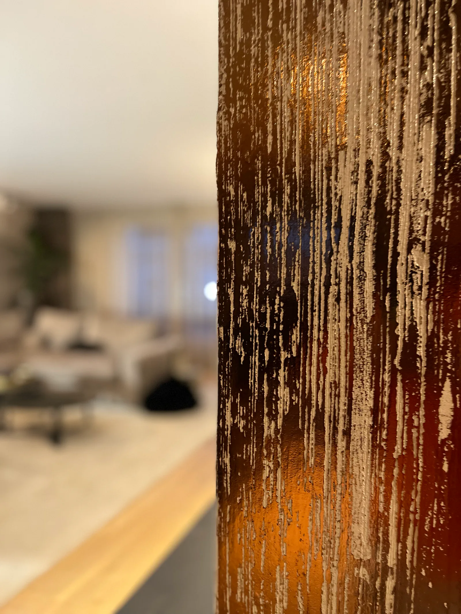 Een donkerbruin wanddetail met lichte verticale reliëflijnen en een warme reflectie, met de ruimte onscherp op de achtergrond.