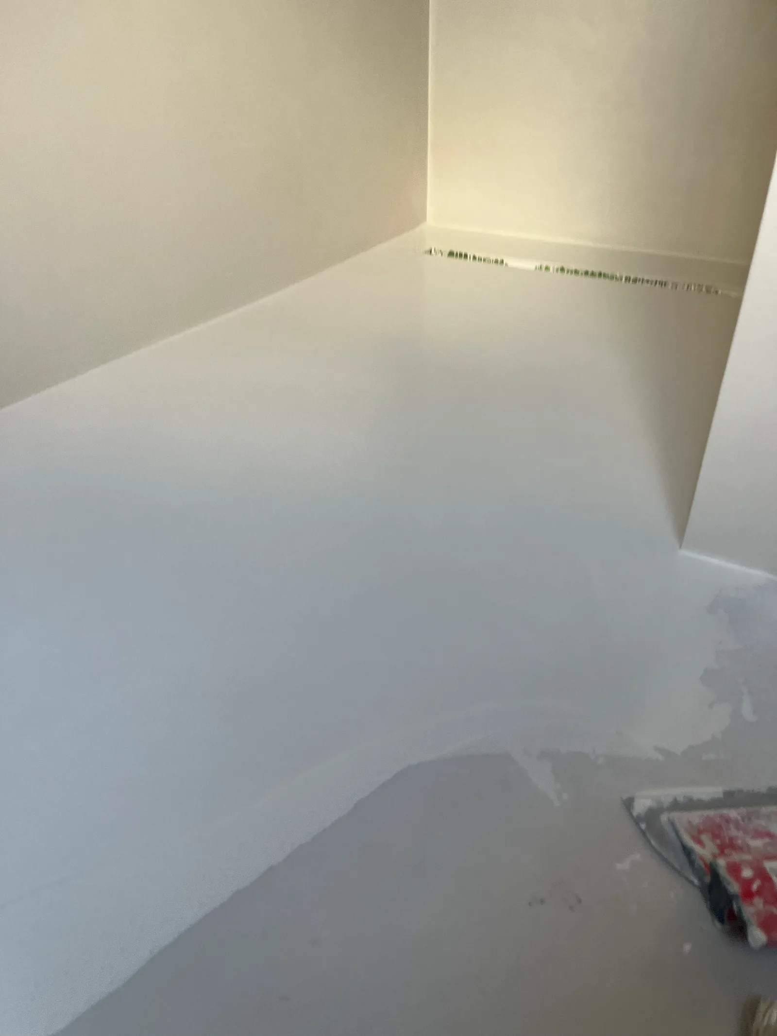 Een lichte laag op een douchevloer, met een spaan op de voorgrond en een afvoer langs de achterwand.