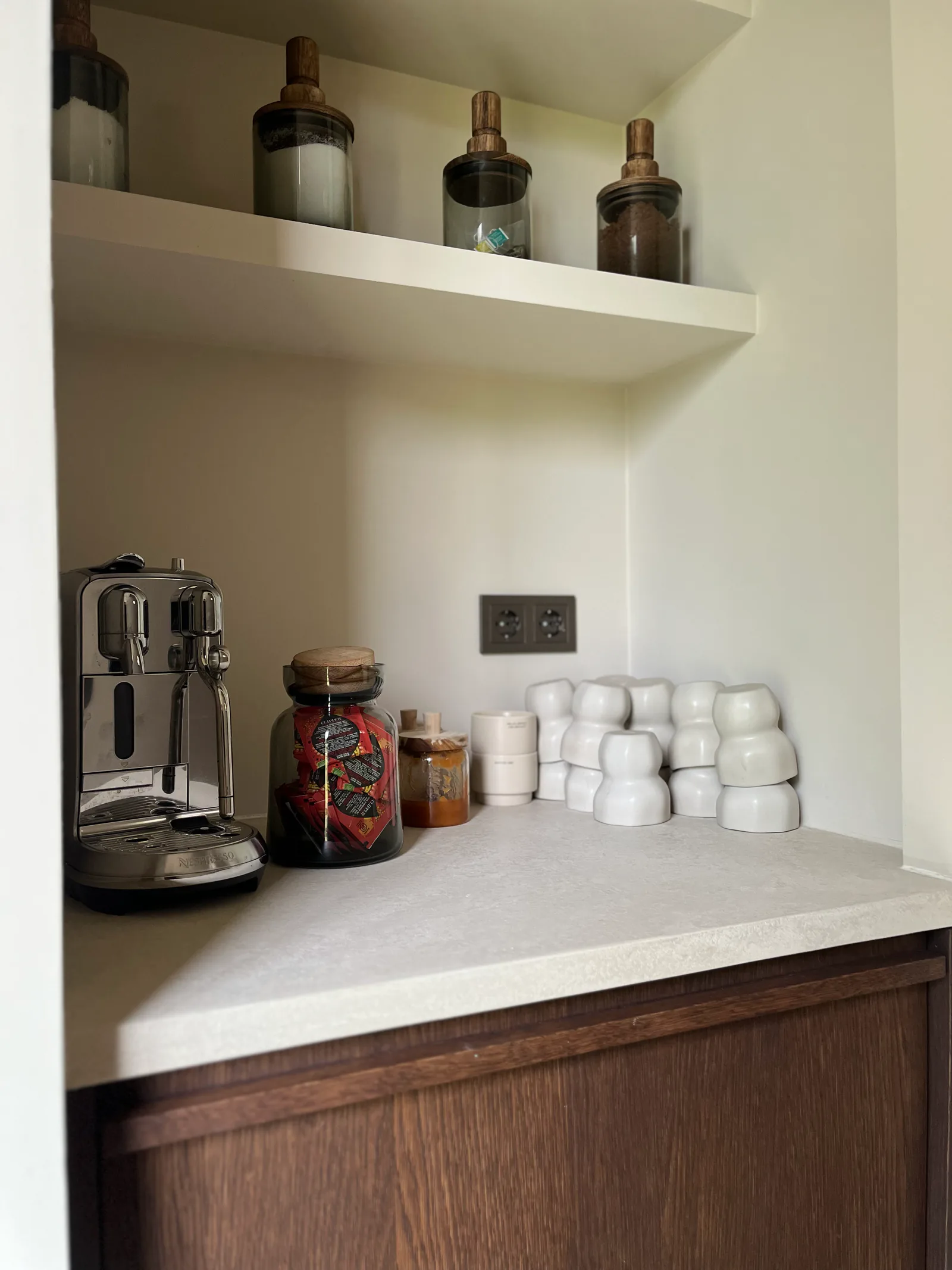 Een koffienis met een licht werkblad, houten onderkast, koffiemachine en kopjes.