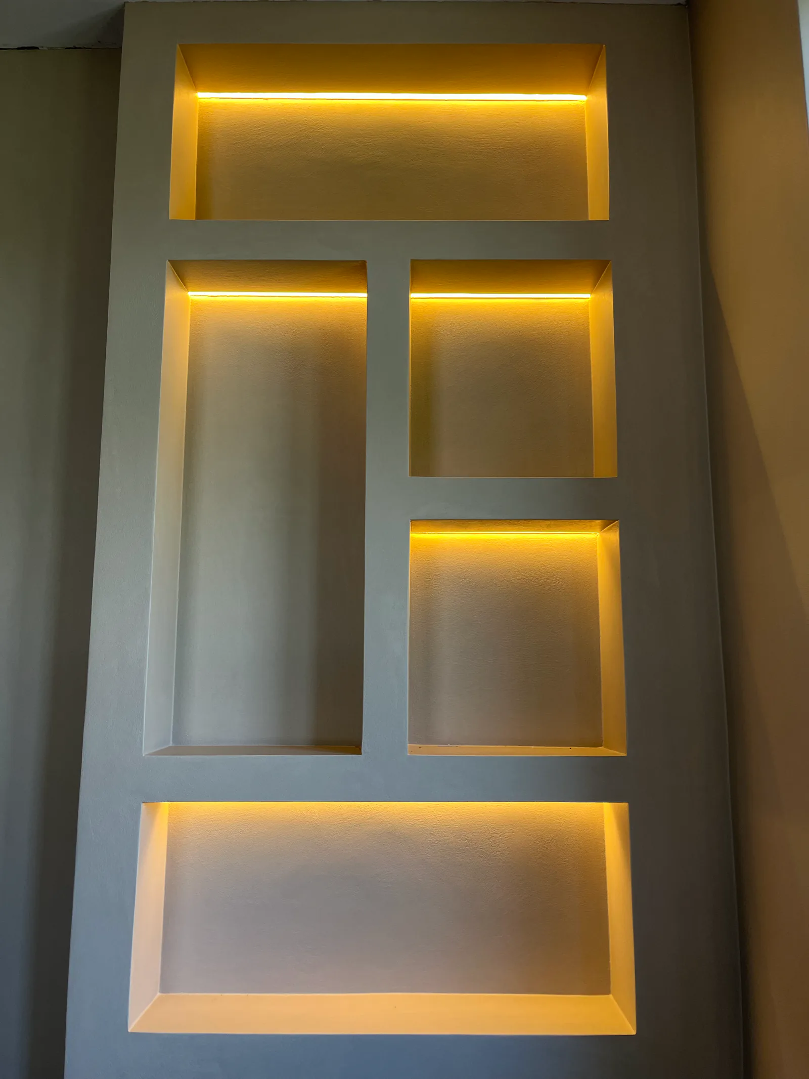 Vijf rechthoekige nissen in een lichte wand, met warme verlichting langs de bovenranden.