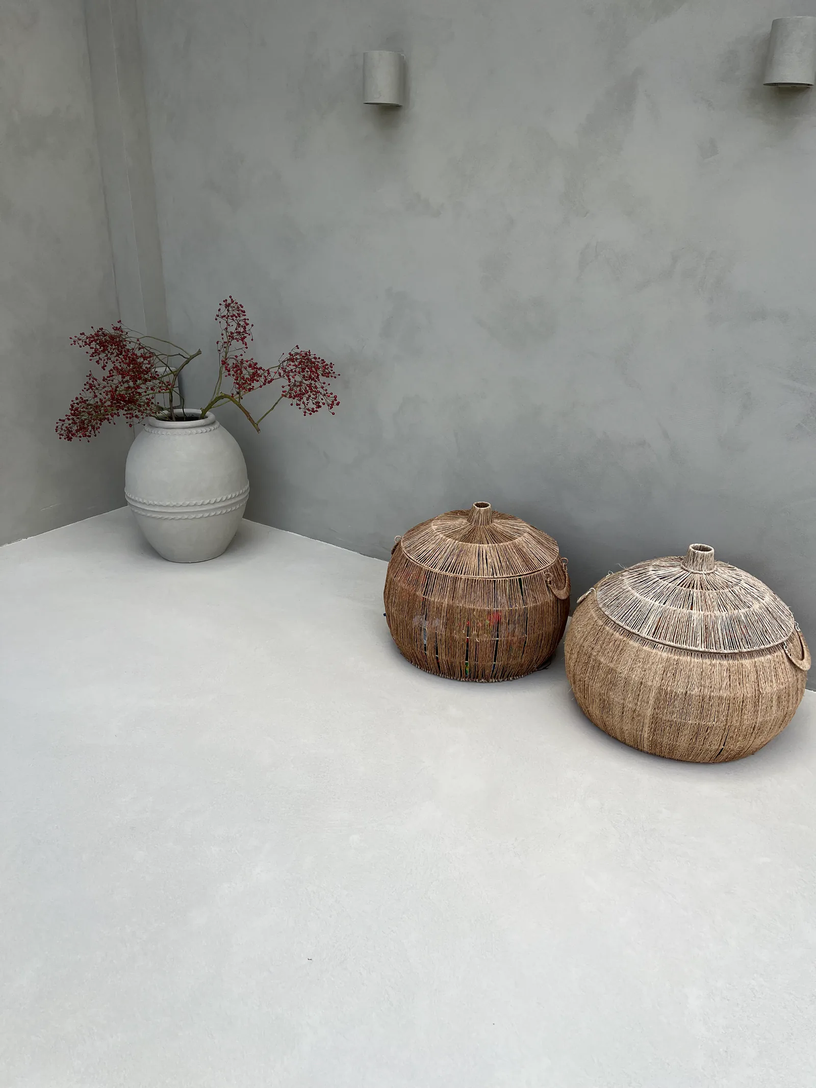 Light microcement floor with woven baskets and a vase beside the sunroom wall