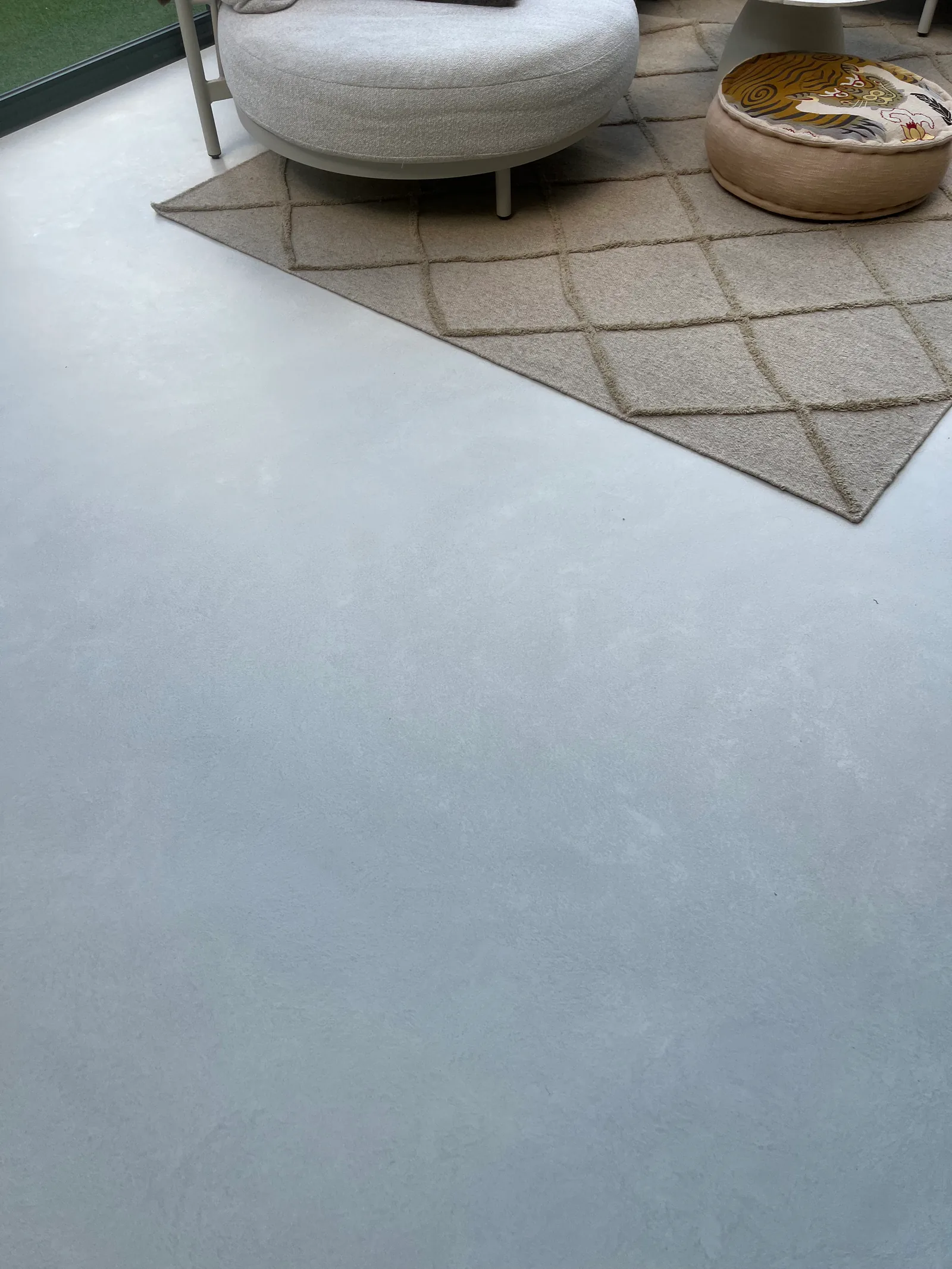 Detail of the Honey 2 microcement floor beside the rug and round armchair