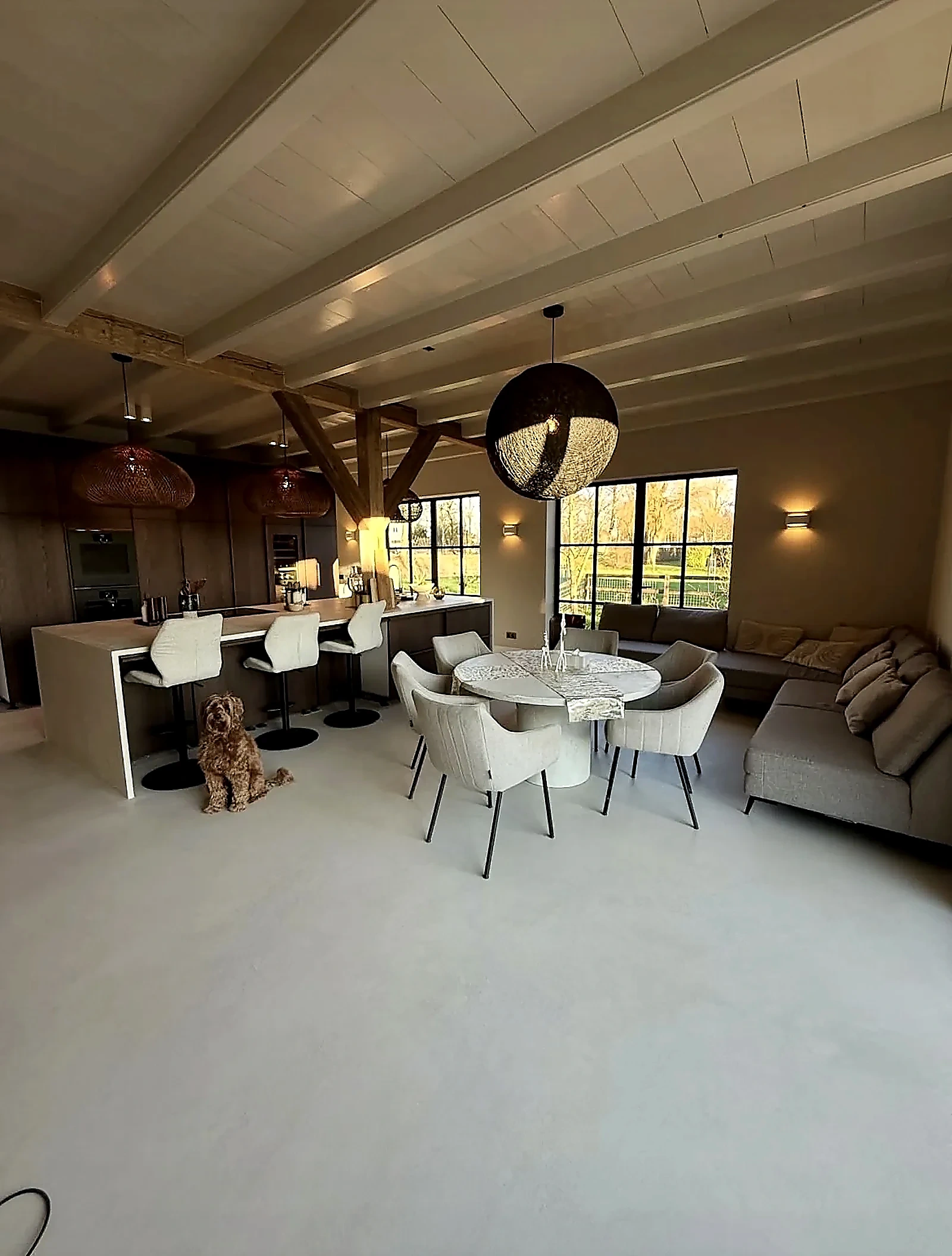 Woonkamer en eethoek met microcement vloer en houten balken in woonboerderij Harmelen