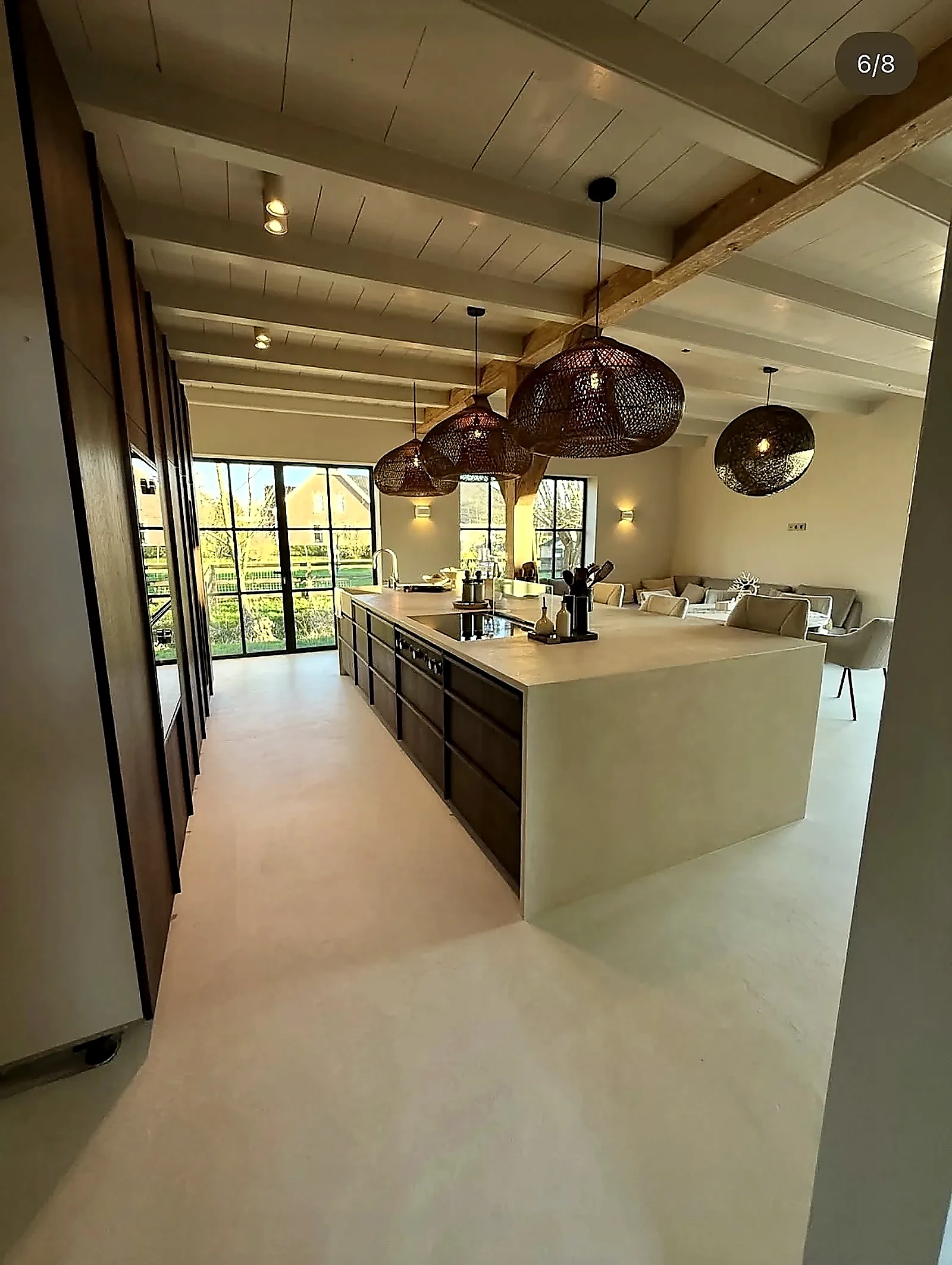 Kitchen island with microcement countertop and seamless floor under rattan pendant lights in farmhouse
